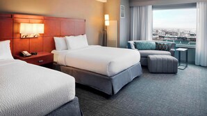 Ein Hotelzimmer mit zwei Betten, einem Schreibtisch und Blick auf die Stadt.