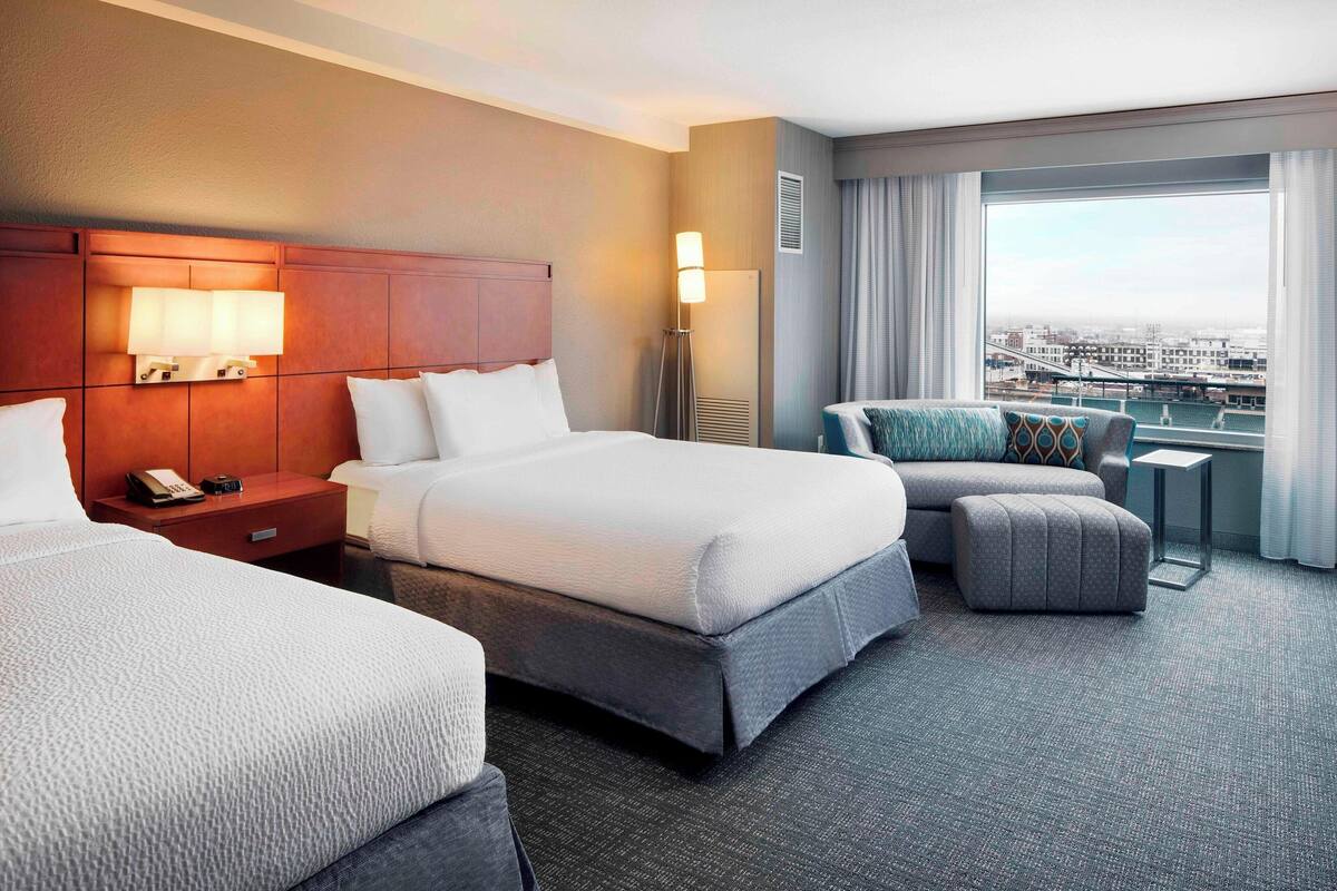 A hotel room with two beds, a desk, and a view of the city.
