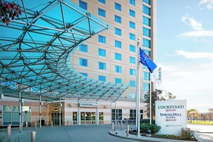 Entrada de un hotel Courtyard Marriott con un toldo de vidrio, una bandera y un letrero que indica SpringHill Suites.