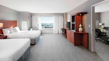 A hotel room with two beds, a desk, a TV, and a view of the city.