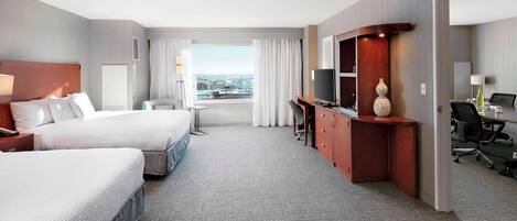 A hotel room with two beds, a desk, a TV, and a view of the city.