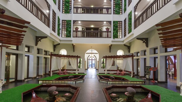 Um saguão de hotel com um elemento central de água, várias varandas e uma entrada imponente.