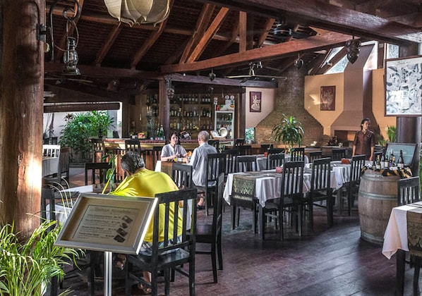 An indoor dining area with wooden beams, tables, chairs, and a bar area with bottles and glasses.