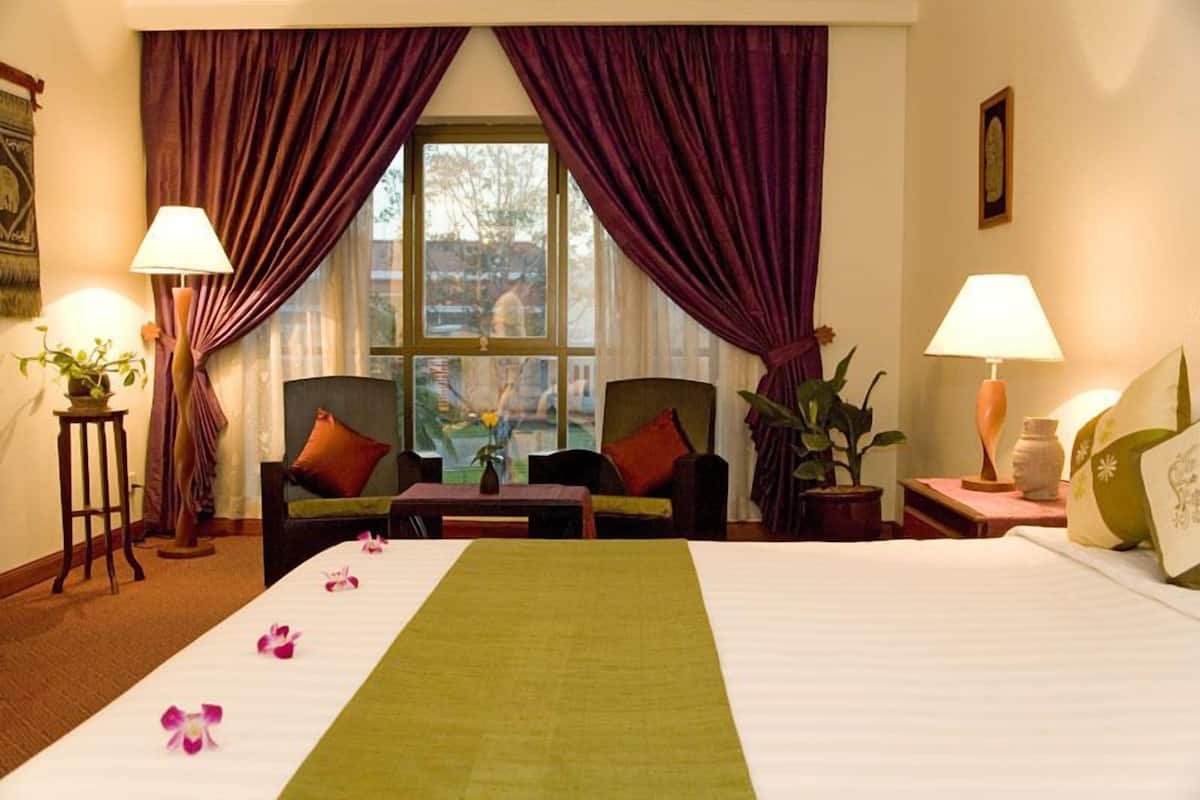 Una habitación de hotel con una cama, dos sillas, una mesa y una ventana con cortinas.