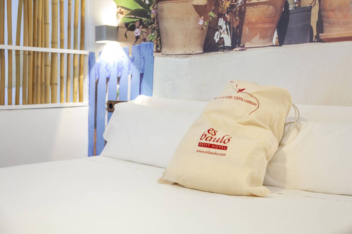 Un lit avec deux oreillers sur lesquels est inscrit « es baulo PETIT HOTEL » et une adresse de site web.