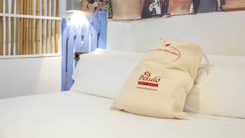 A bed with two pillows, one labeled "es baulo PETIT HOTEL" and the other "100% cotton."