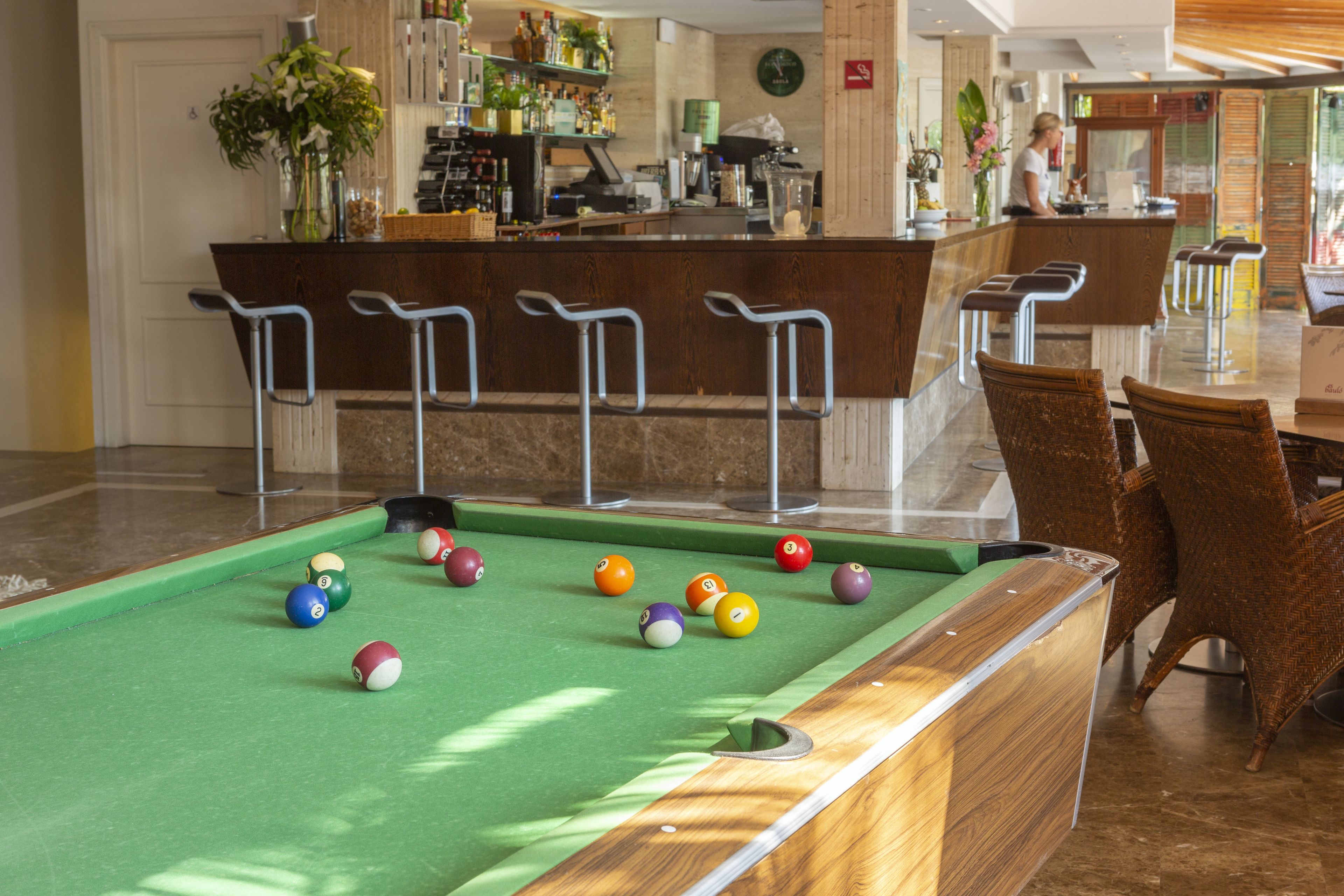Een pooltafel met ballen, een bar met krukjes en een zithoek met stoelen.