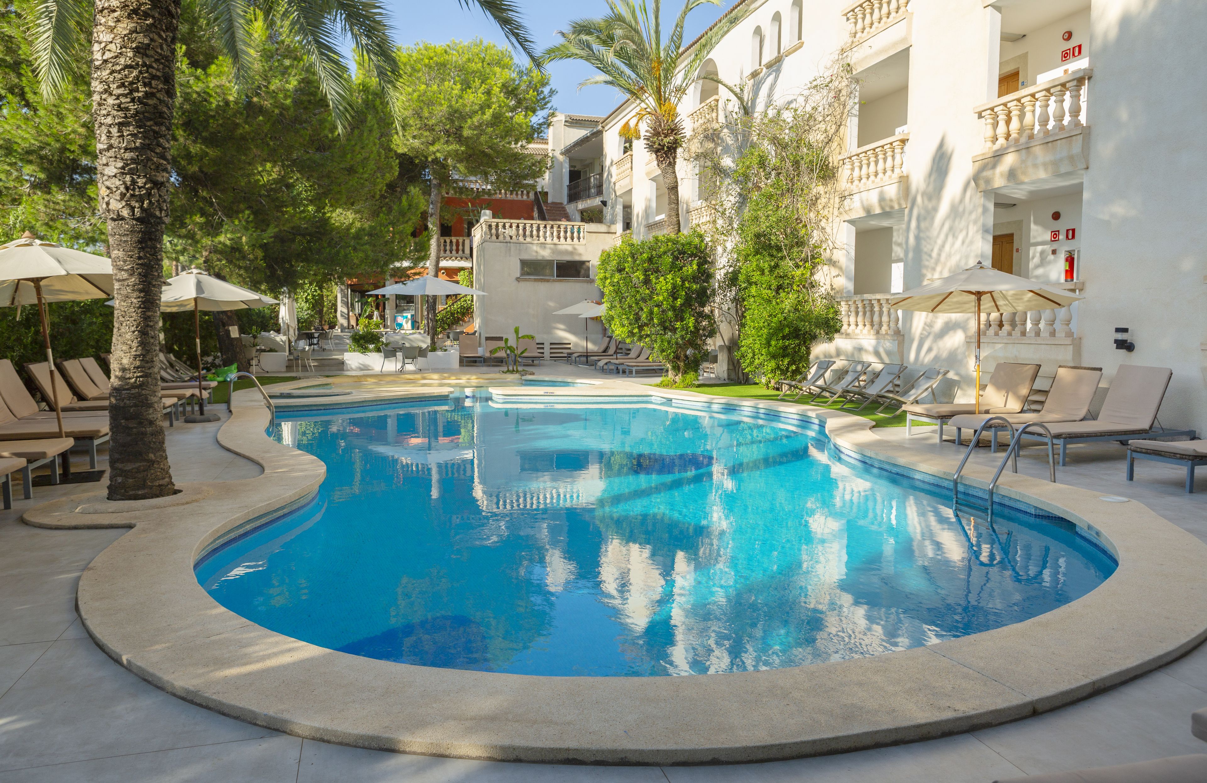 Una piscina rodeada de sillas de descanso y sombrillas, con un edificio al fondo.