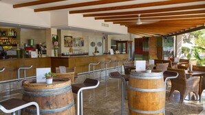 A bar area with wooden barrels, metal stools, and a counter with various bottles.