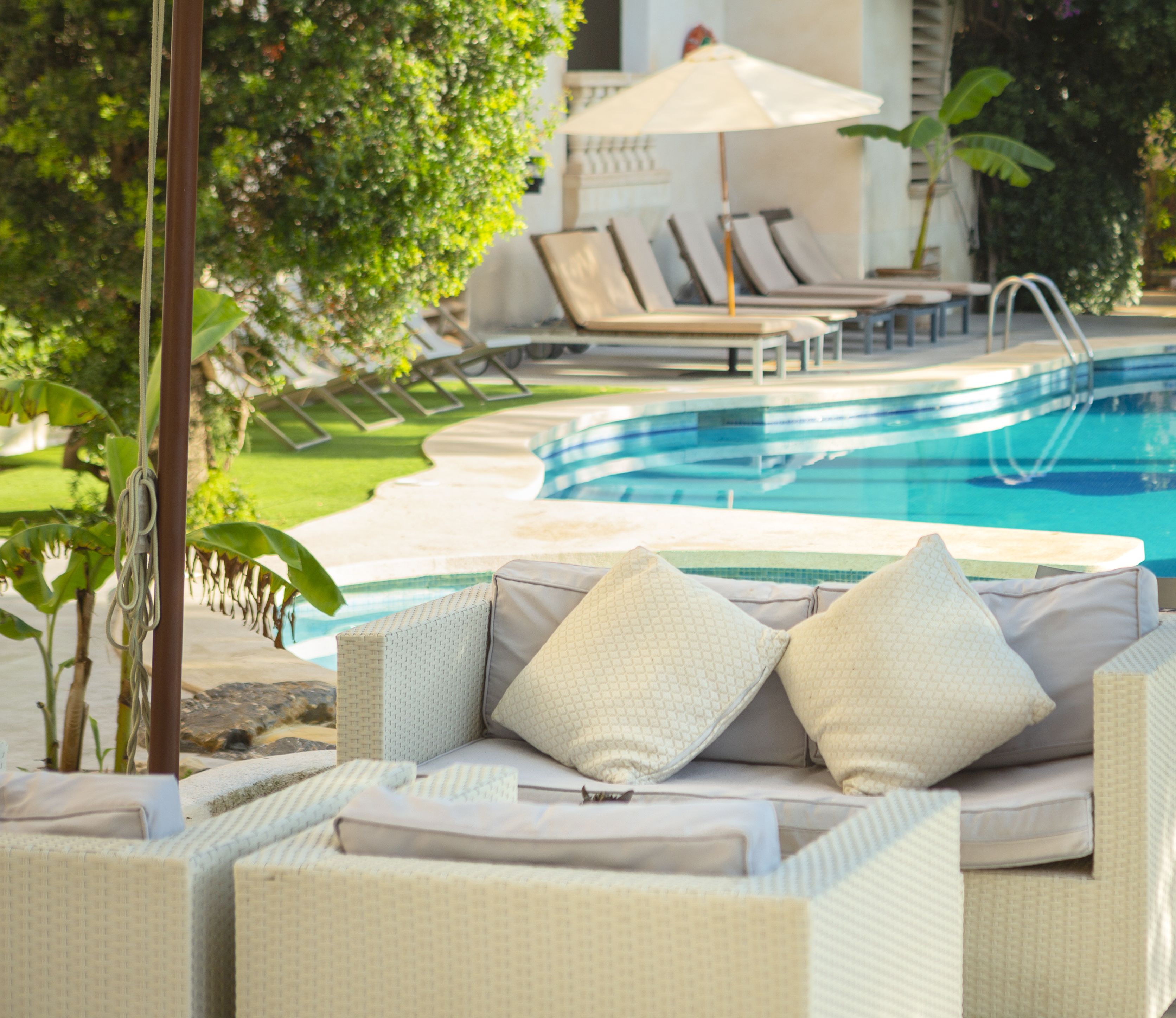 Un espace aménagé au bord de la piscine, avec un canapé en osier, des chaises longues et une piscine.