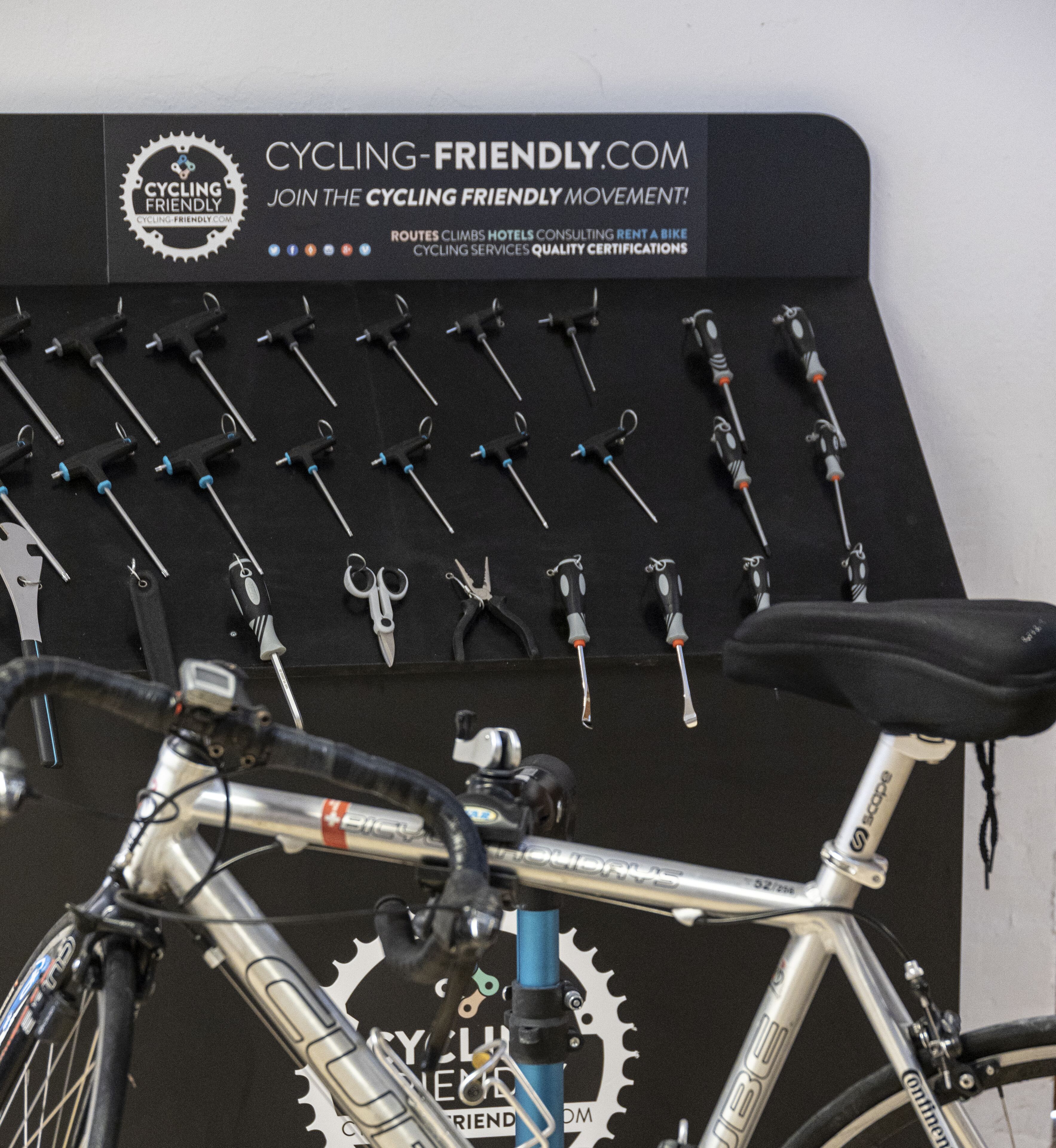 Una bicicleta con un sistema de cambios y un asiento negro, ubicada frente a una pared que muestra diversas herramientas para bicicletas y un cartel que anuncia servicios para ciclistas.