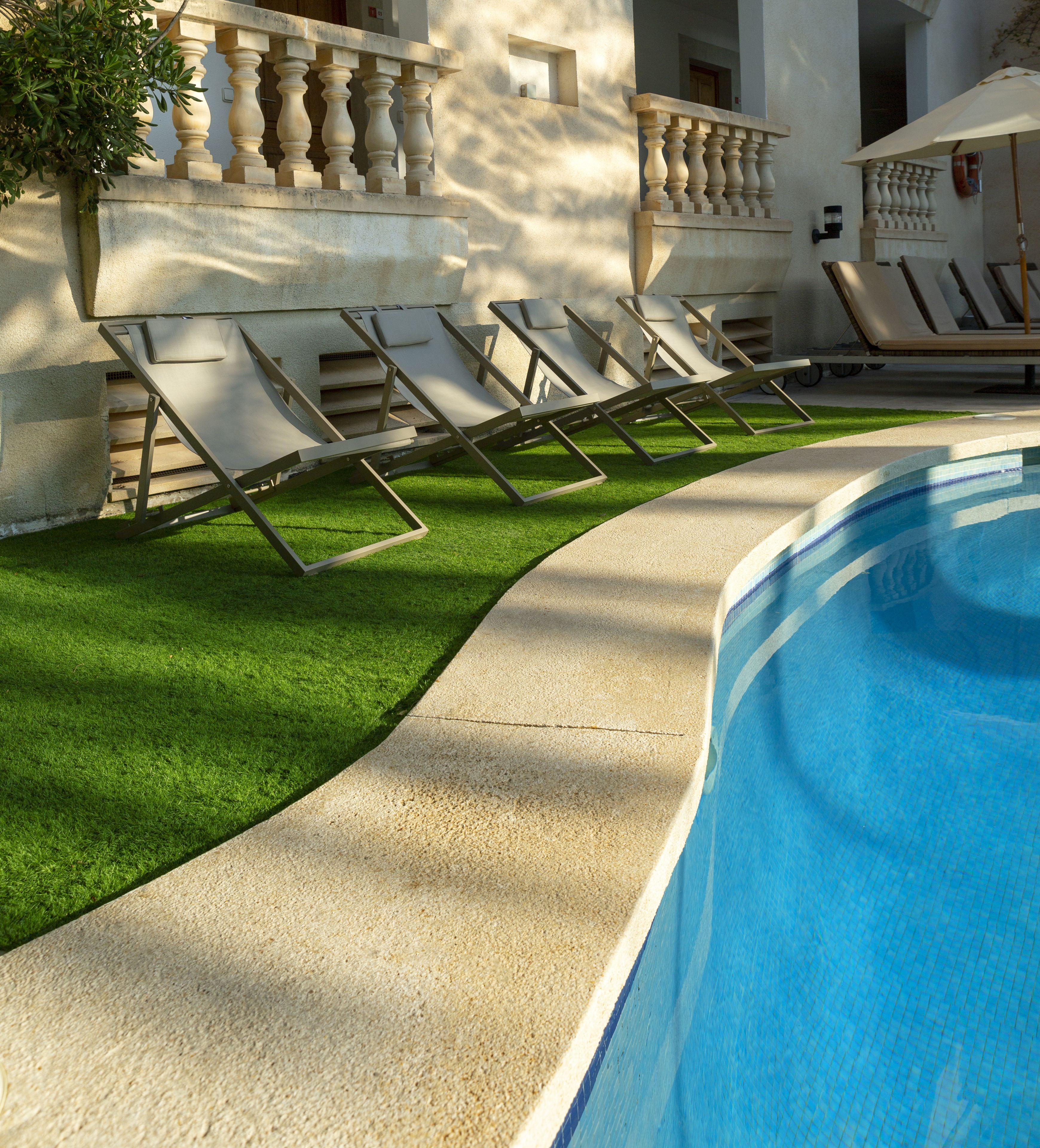 Un área junto a la piscina con sillones de descanso, un camino de hormigón y una pileta.