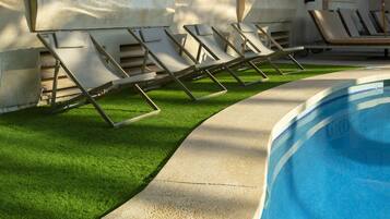 Un área junto a la piscina con sillones de descanso, un camino de hormigón y una pileta.