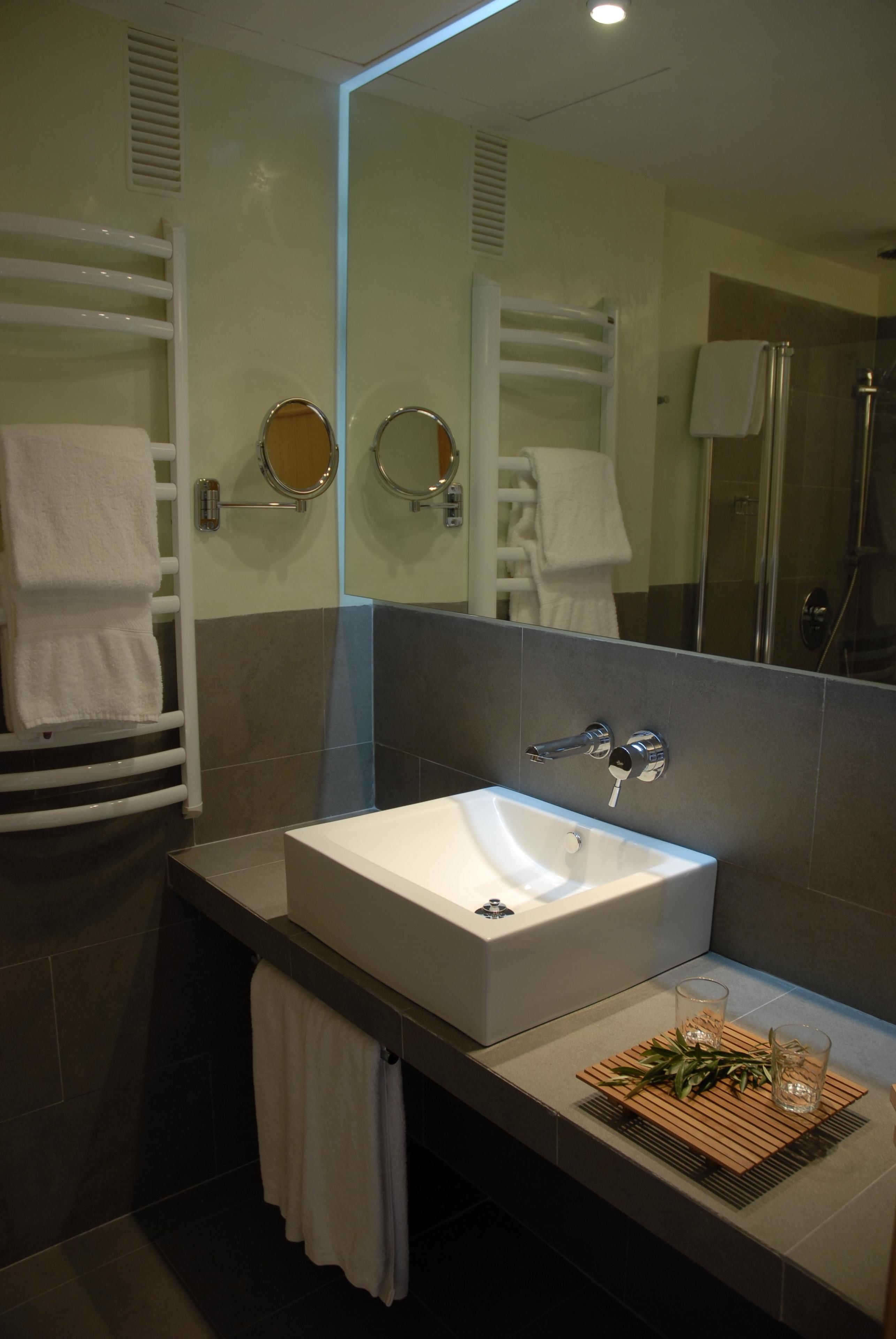 A modern bathroom with a large mirror, a white sink, and a glass shower enclosure.