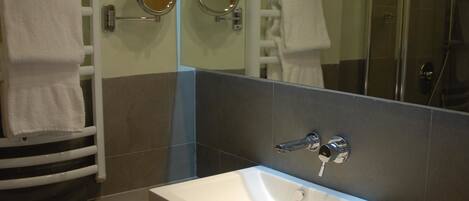 Un baño moderno con un espejo grande, un lavabo blanco y una cabina de ducha de vidrio.