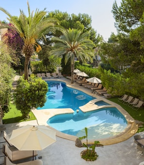 Une piscine dotée de plusieurs espaces de détente, de palmiers et d’un jardin bien entretenu.