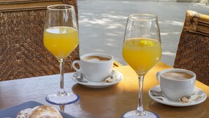 A table with two white cups of coffee and two glasses of orange juice, a plate with pastries, and wicker chairs.