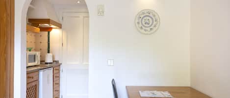 A kitchen with a microwave, toaster, and refrigerator, an archway leading to another room, and a dining table with chairs.