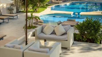Zona de piscina con sillones, un sofá y una pequeña mesa con una planta.