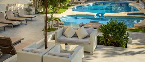Zona de piscina con sillones, un sofá y una pequeña mesa con una planta.
