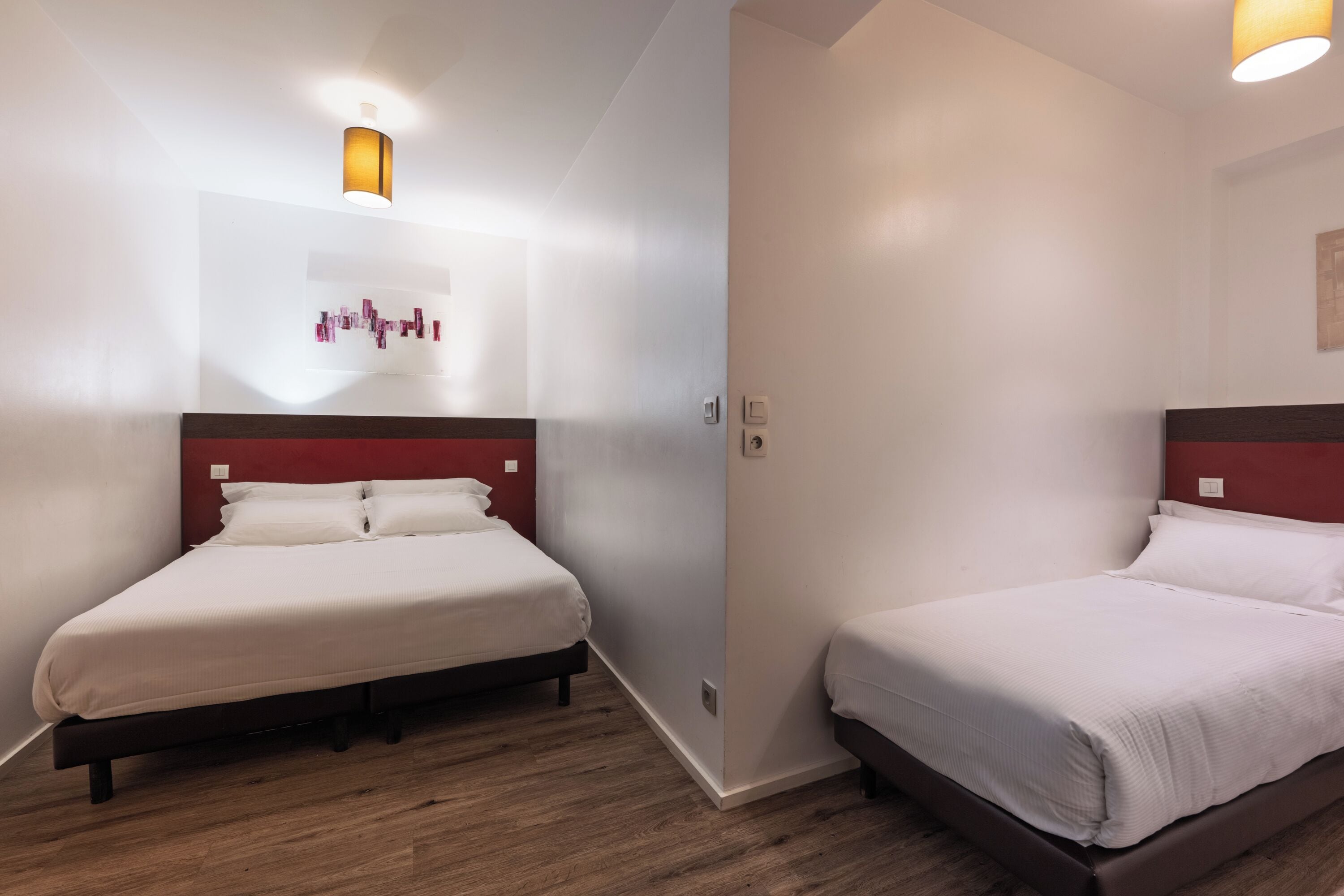 A hotel room with two beds, wooden flooring, and a red accent wall.