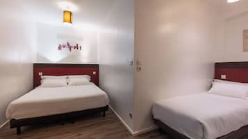 A hotel room with two beds, wooden flooring, and a red accent wall.