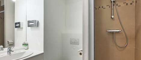 A bathroom with a white sink, mirror, and toilet, and a shower area with brown tiles.