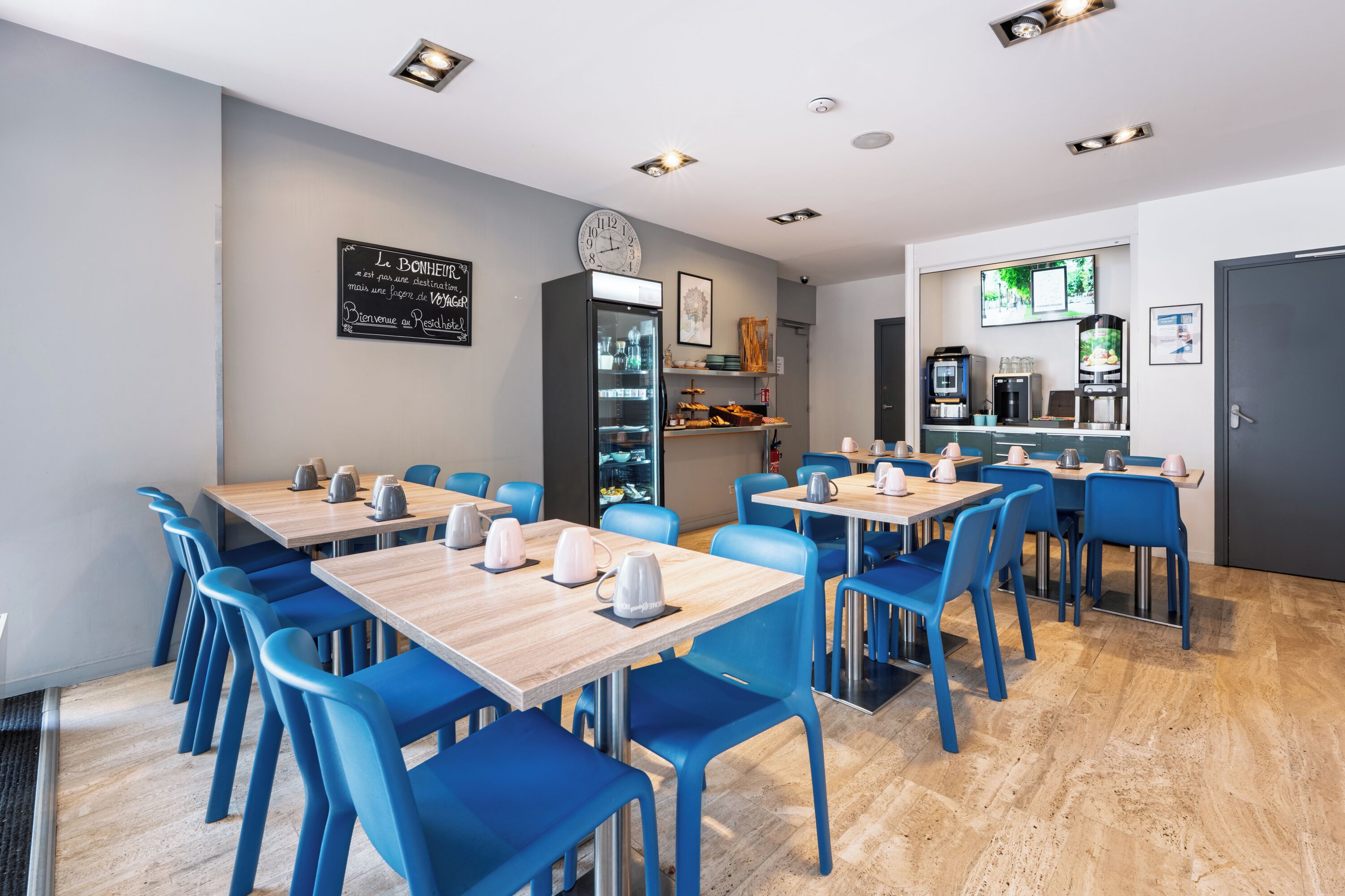 A modern restaurant with blue chairs and wooden tables, a clock on the wall, and a coffee machine.