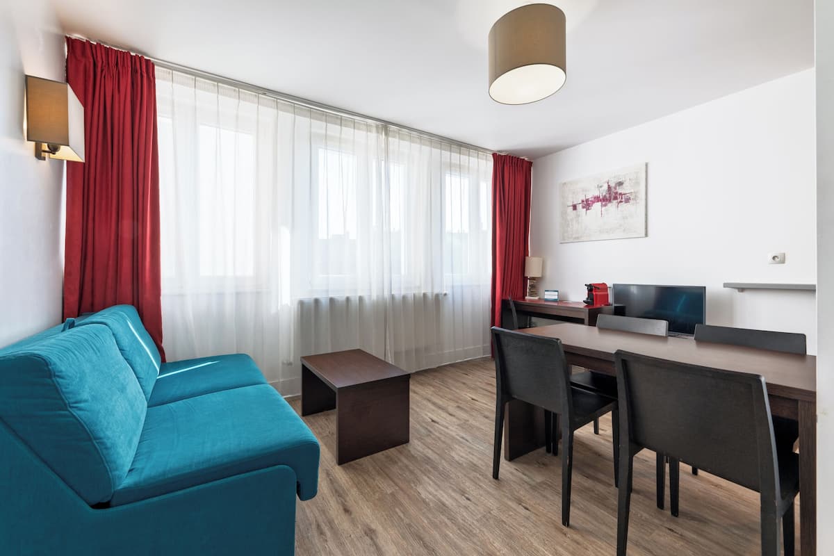 A modern living room with a sofa, a dining table with chairs, a TV, and a coffee machine.
