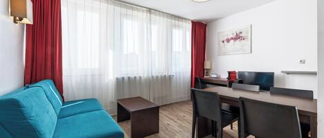 A modern living room with a sofa, a dining table with chairs, a TV, and a coffee machine.