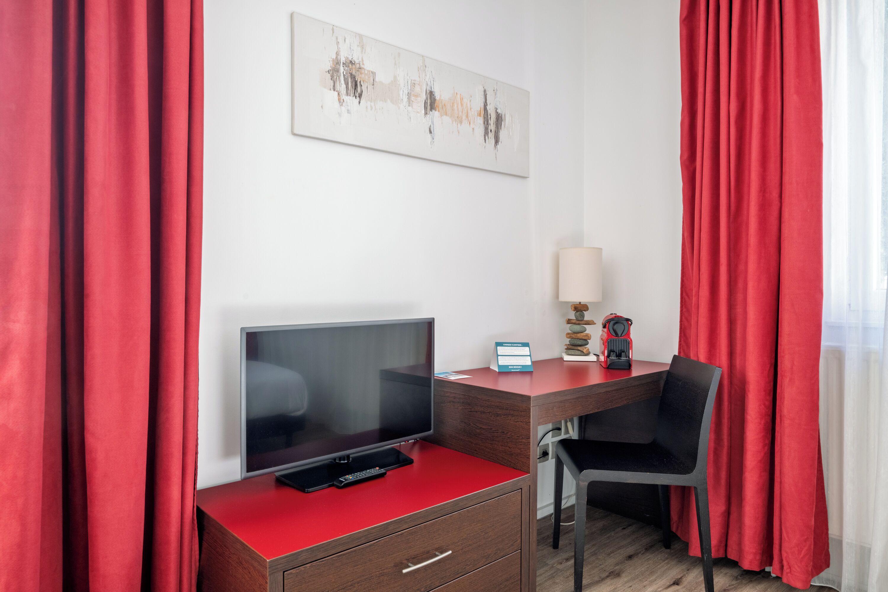 A hotel room with a red desk, a television, a lamp, and a chair.
