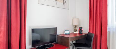 Una habitación de hotel con un escritorio rojo, un televisor, una lámpara y una silla.