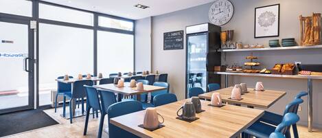 Una cafetería moderna con mesas de madera y sillas azules, un reloj grande y un menú en la pizarra.