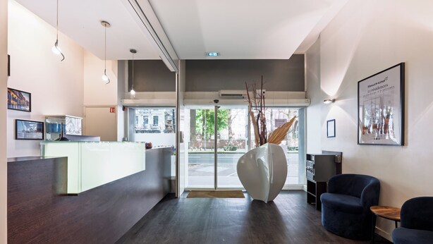 A modern hotel reception area with a wooden reception desk, a large abstract sculpture, and a seating area with dark blue chairs. - Residhotel Lille Vauban (Lille)