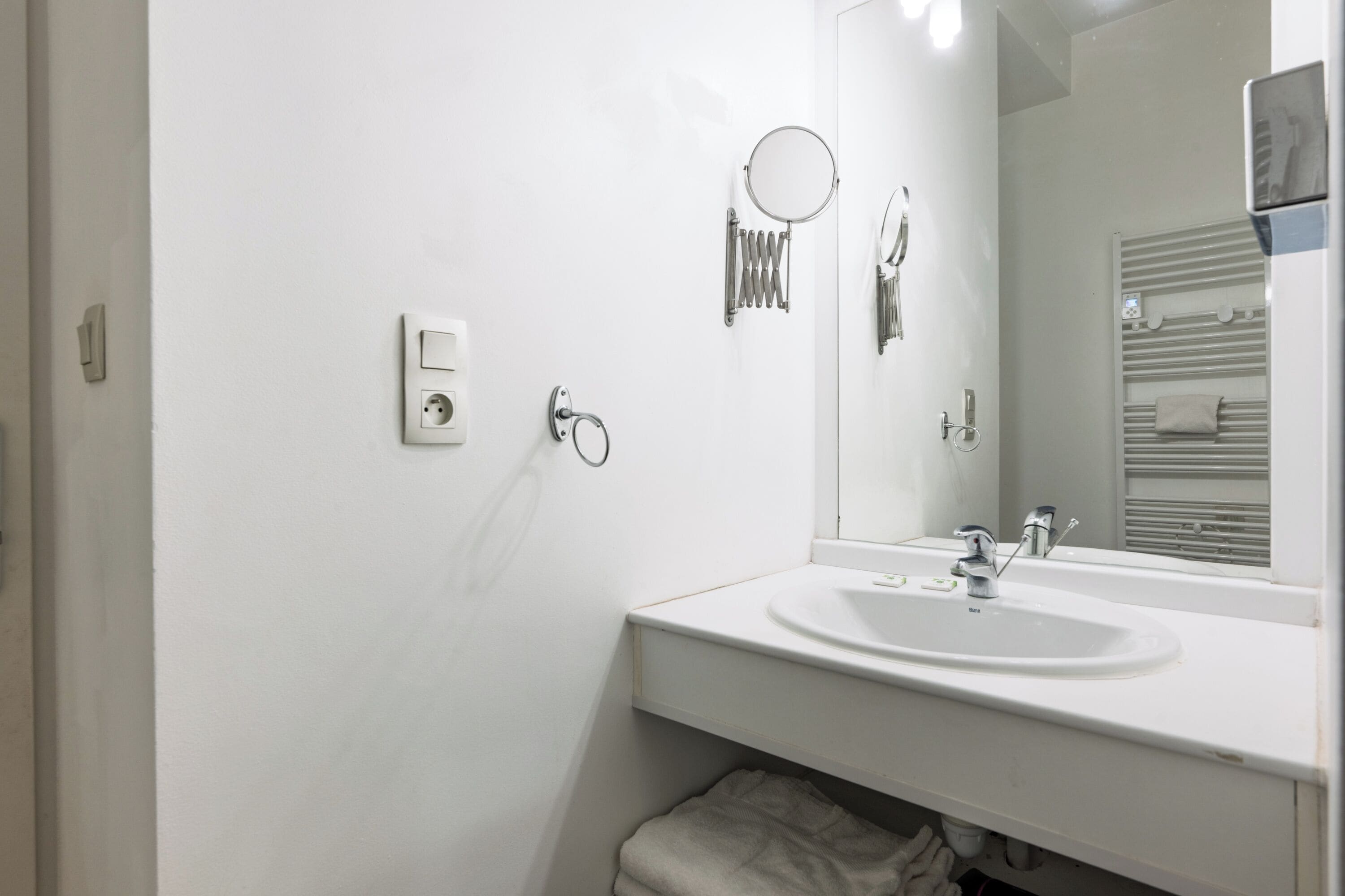 Une salle de bain moderne avec un lavabo blanc, un miroir et un porte-serviettes.