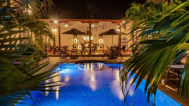 A swimming pool with surrounding lounge chairs and umbrellas, set against a building with a tiled roof. - Hotel Plaza Colon (Granada)