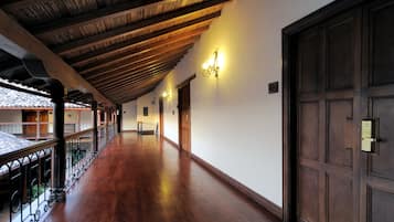 Un pasillo con piso de madera, un balcón con baranda y una puerta grande de madera.