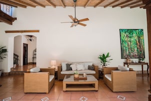 Amplia sala de estar con ventilador de techo, un conjunto de sofás, una mesa de centro y un cuadro en la pared.