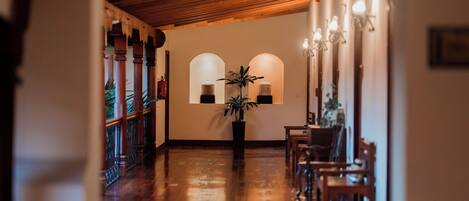 Un pasillo con suelo de madera, una planta en maceta y un área de descanso con sillas y una mesa.