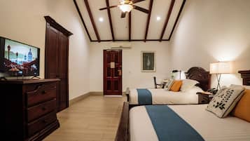 A hotel room with a wooden ceiling, a television, a desk with a lamp, two beds with pillows, and a door.
