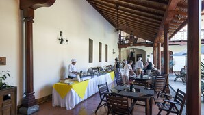 A covered outdoor dining area with wooden tables and chairs, a buffet setup, and a view of the interior. - Hotel Plaza Colon (Granada)