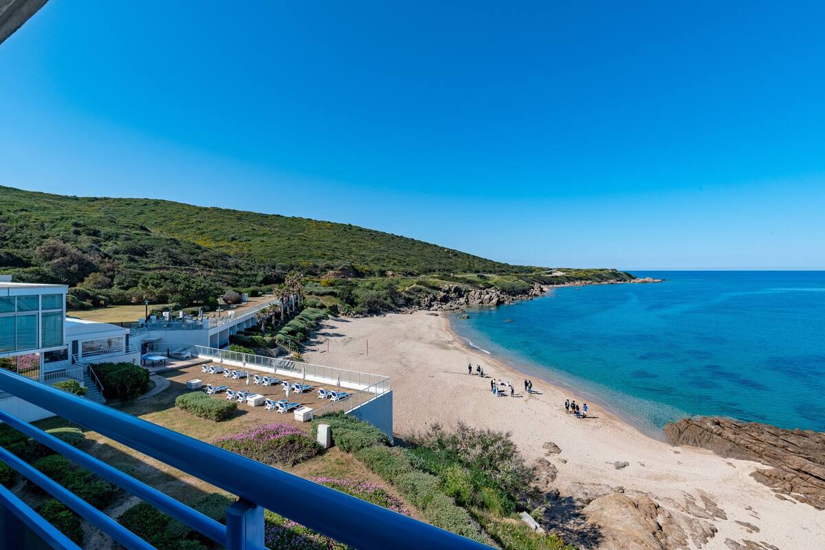 Une plage offrant une vue dégagée sur l’océan, un bâtiment doté d’un espace piscine et une colline verdoyante.