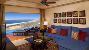 Un salon avec un canapé bleu, une table basse, un téléviseur et une vue sur l’océan.