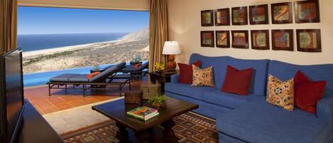 A living room with a blue sofa, a coffee table, a TV, and a view of the ocean.