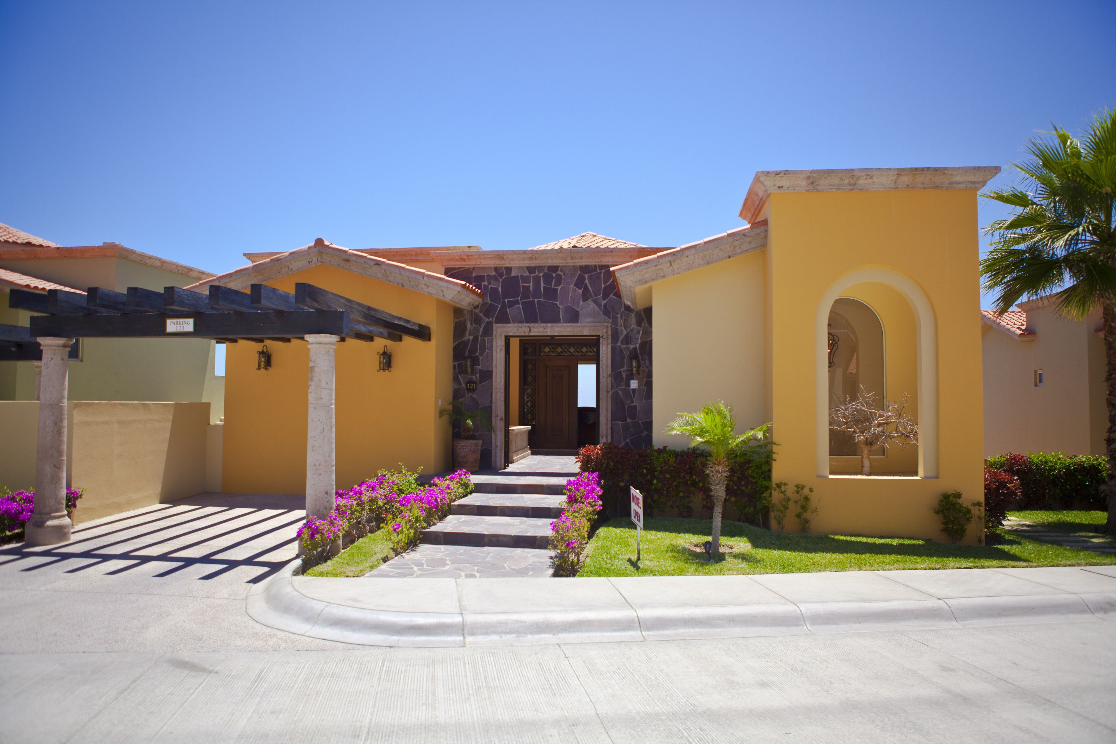 A residential building with a stone entrance, a covered patio, and a well-maintained garden with flowers.