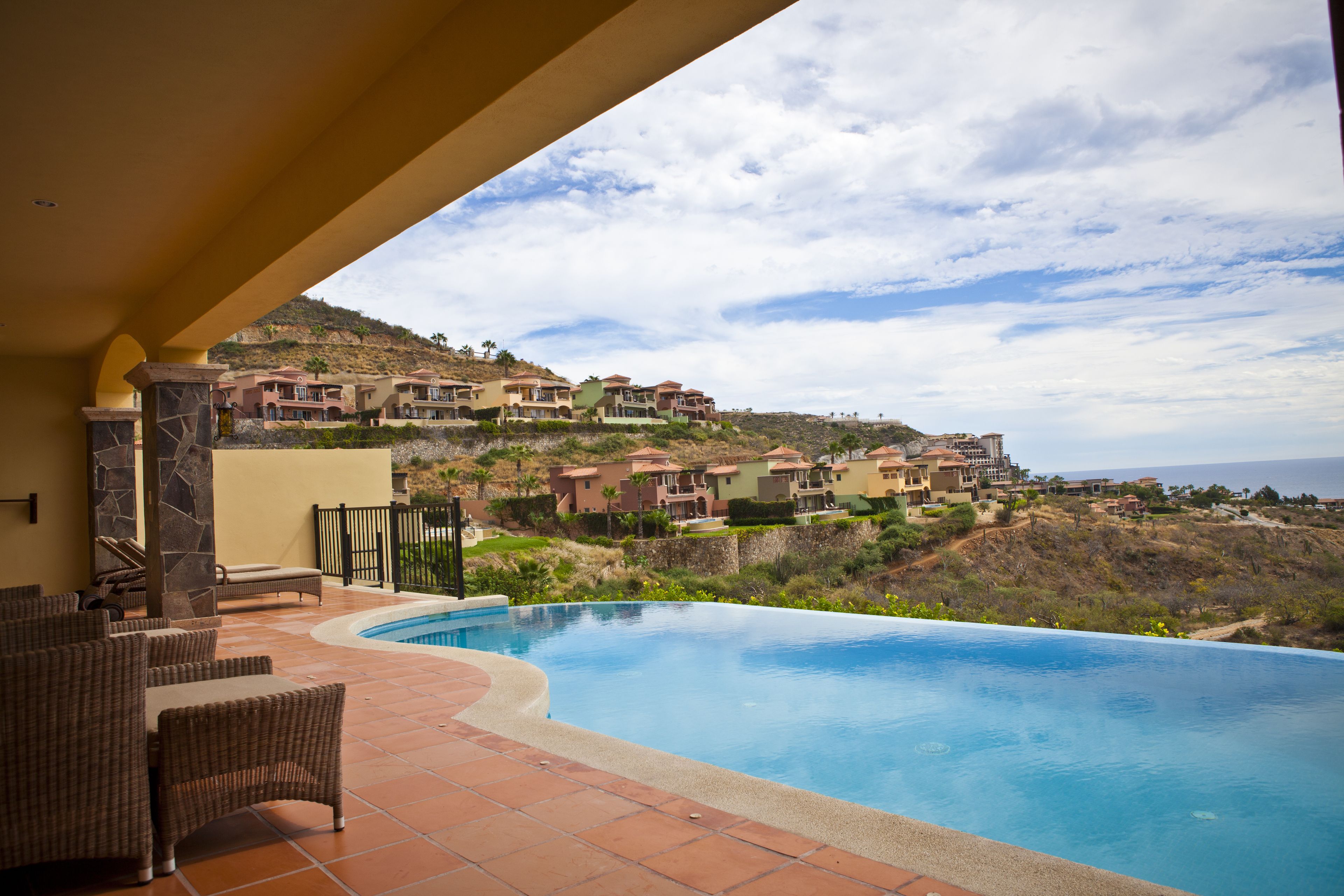 Zona de piscina con mobiliario exterior, vistas a edificios en la colina y cielo despejado.