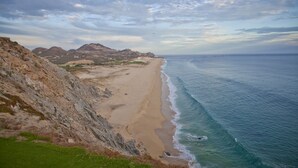 Un paysage côtier avec une plage de sable, des falaises rocheuses et une vue sur l’océan.
