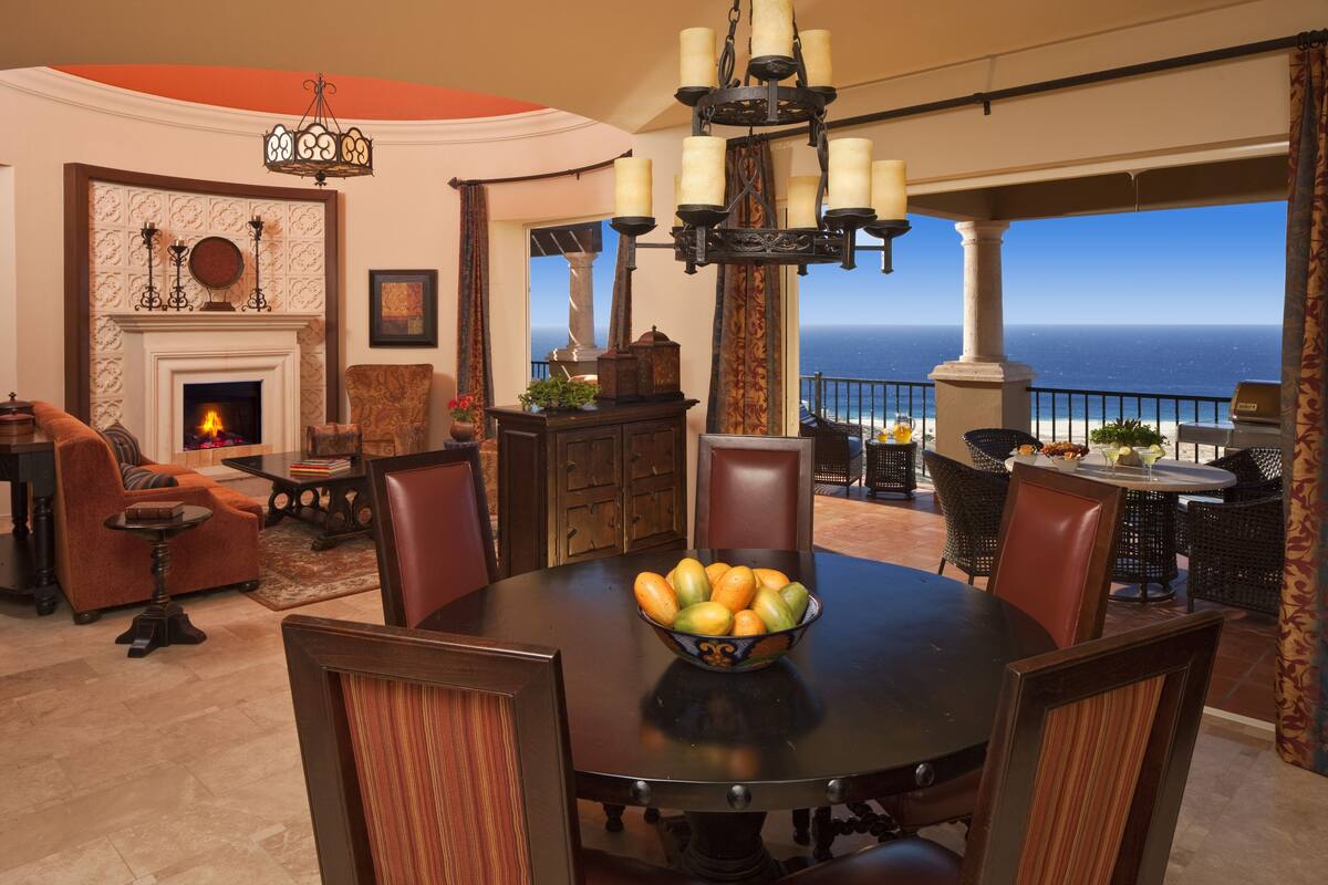 A dining area with a round table, chairs, a fruit bowl, and a fireplace.