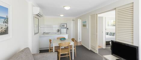 Un espacio habitable compacto con kitchenette, zona de comedor, área de descanso con sofá y sillas, y televisor sobre un mueble.