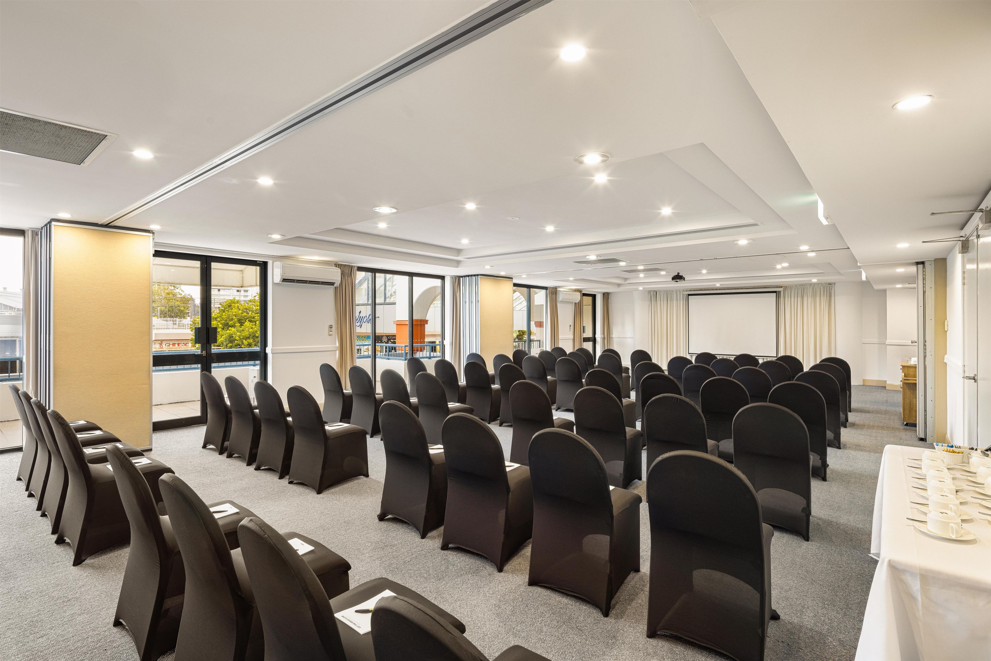 A conference room with rows of chairs, a projector screen, and a table with a white tablecloth.